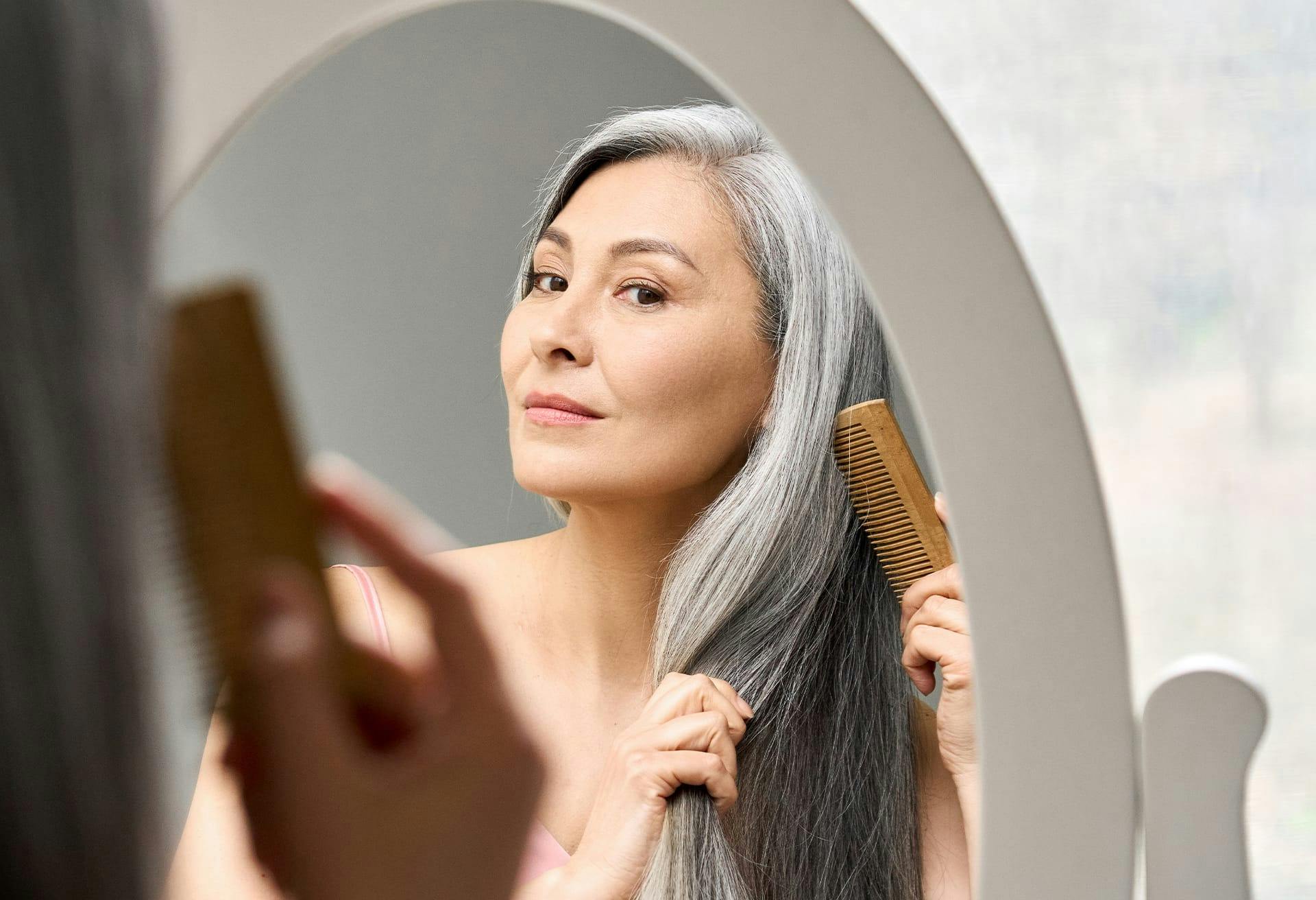 Woman looking in a mirror while brushing her long grey hair