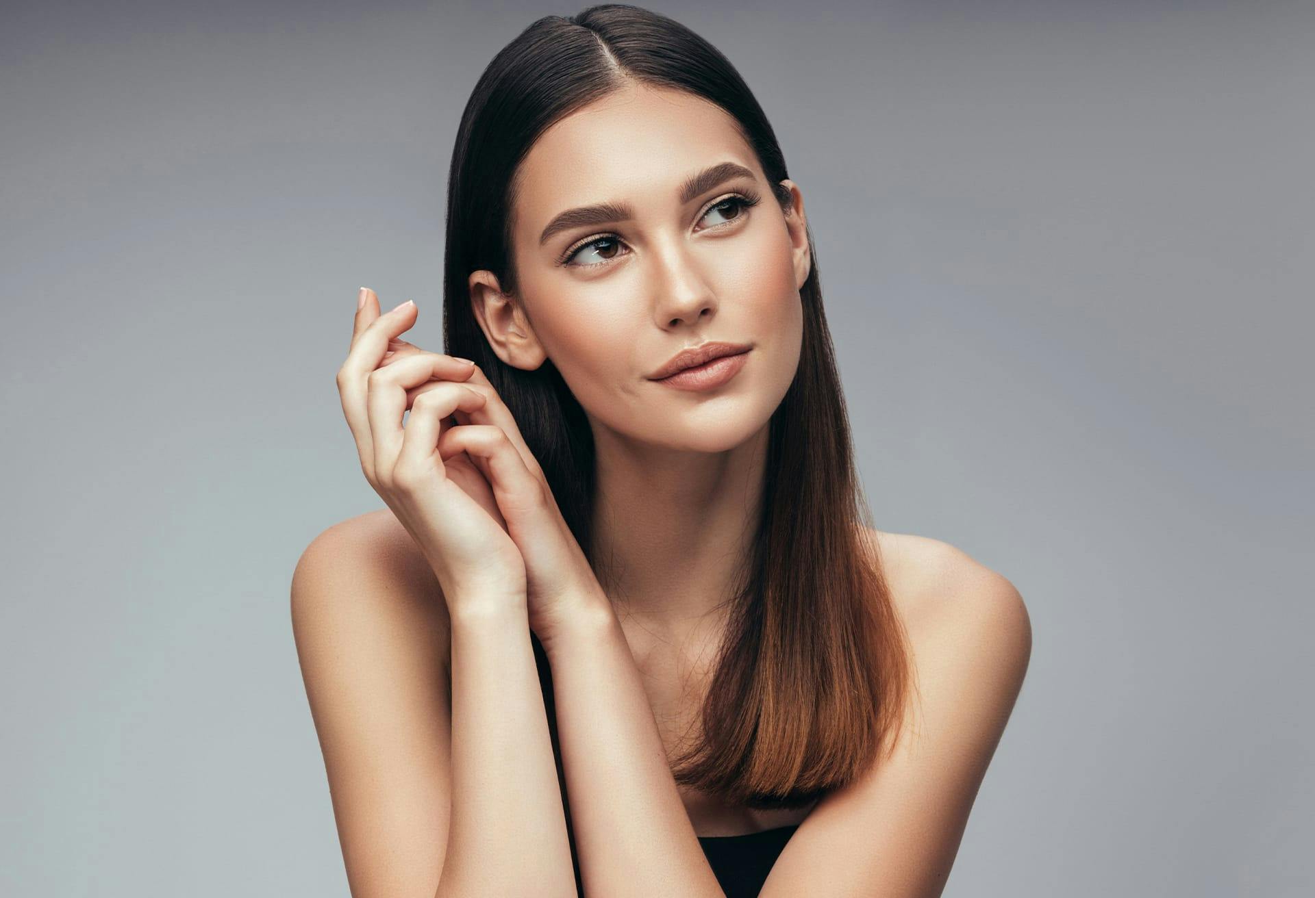 Woman with long straight brown hair folding her hands together near her face