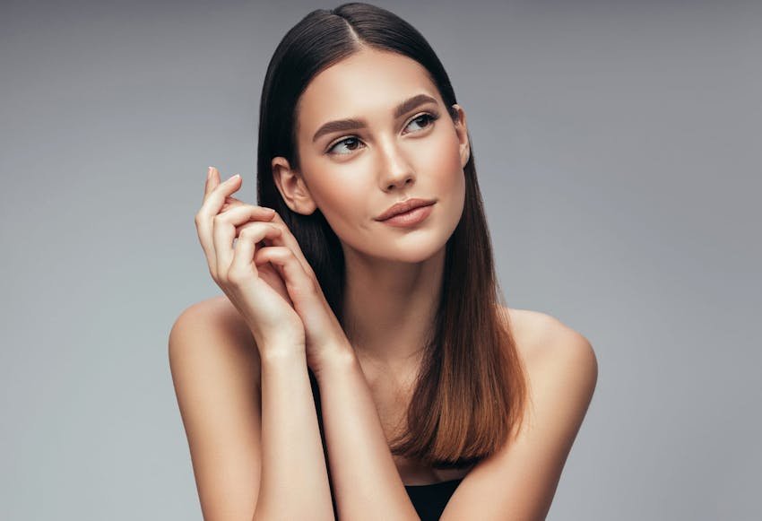 Woman with long straight brown hair folding her hands together near her face