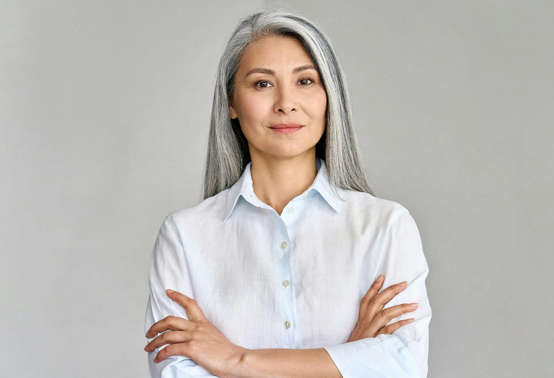 Woman with long grey hair wearing a long sleeve white button up shirt