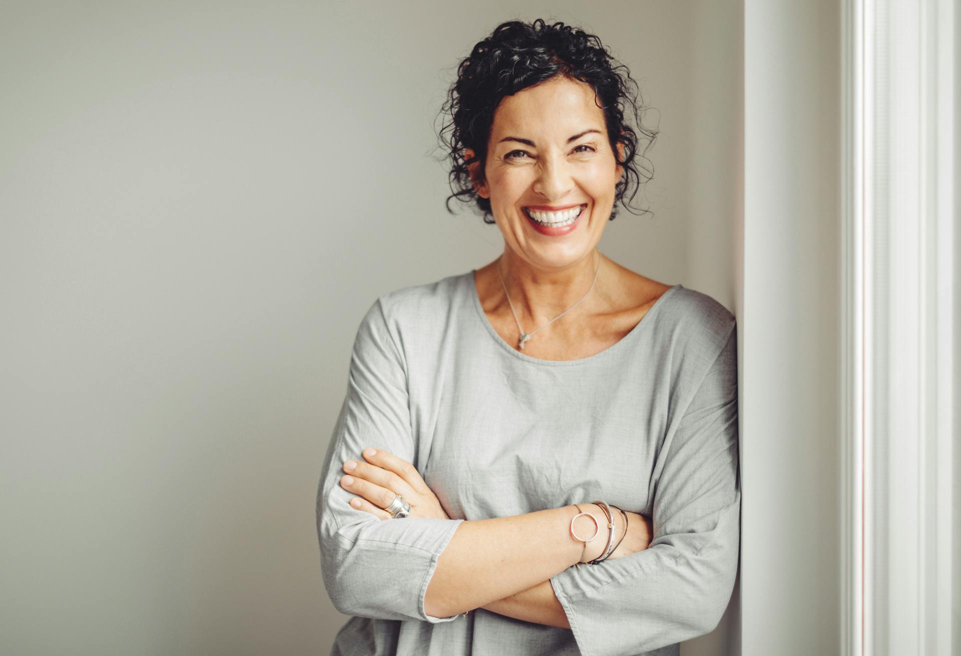 Woman smiling wearing a grey shirt with her arms crossed