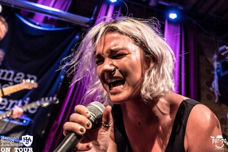 Zangeres die met volle emotie in close up op een paars/roze podium van de HBA in een microfoon zingt.