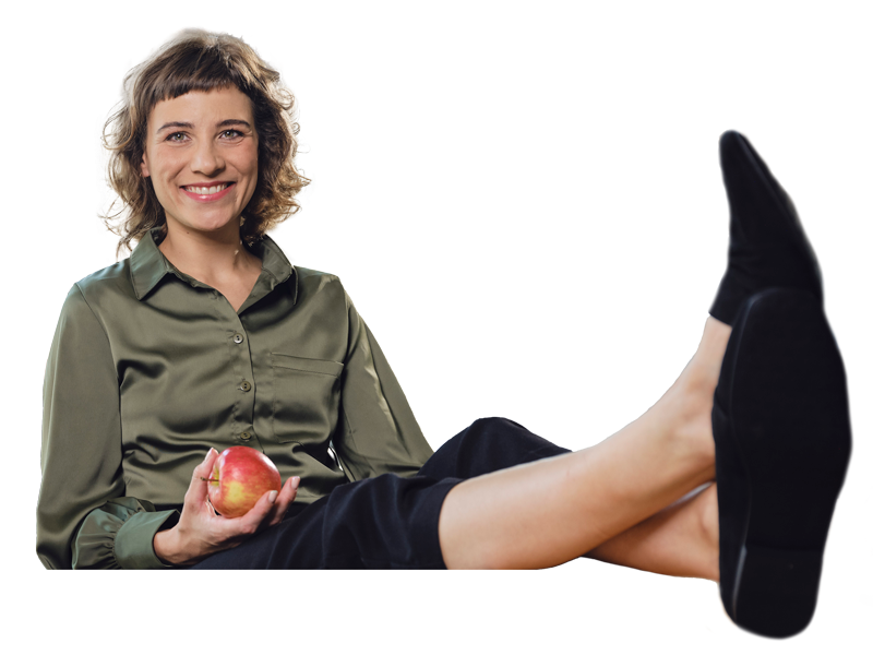 Eine junge Frau sitzt lächelnd mit einem Apfel in der Hand auf einem Stuhl. Legen auch Sie Ihr Geld richtig an und sparen Sie in Edelmetalle mit den Sparplänen von Golden Gates.
