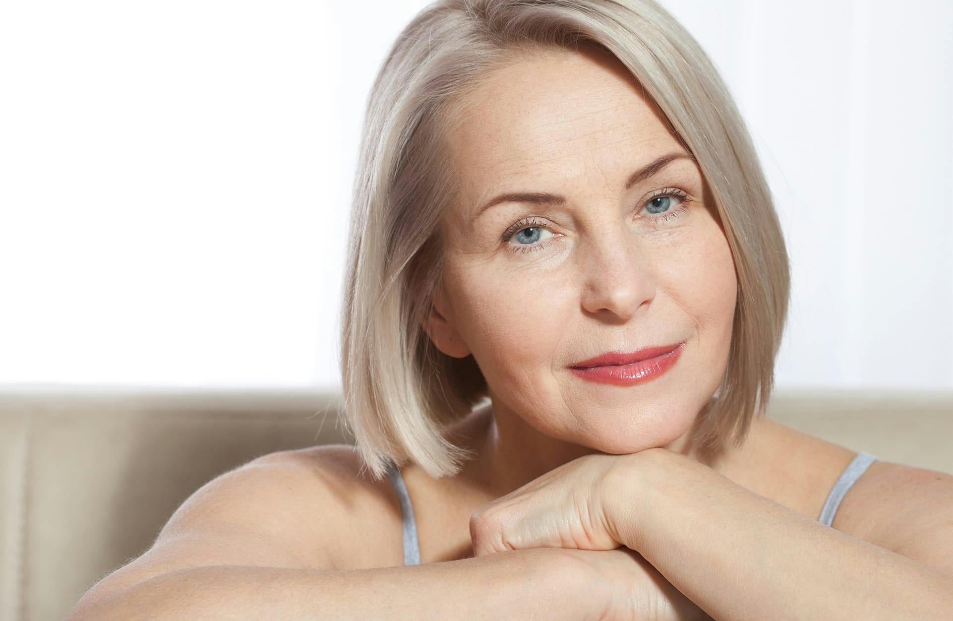 older woman with grey/blonde hair resting her chin on her folder hands
