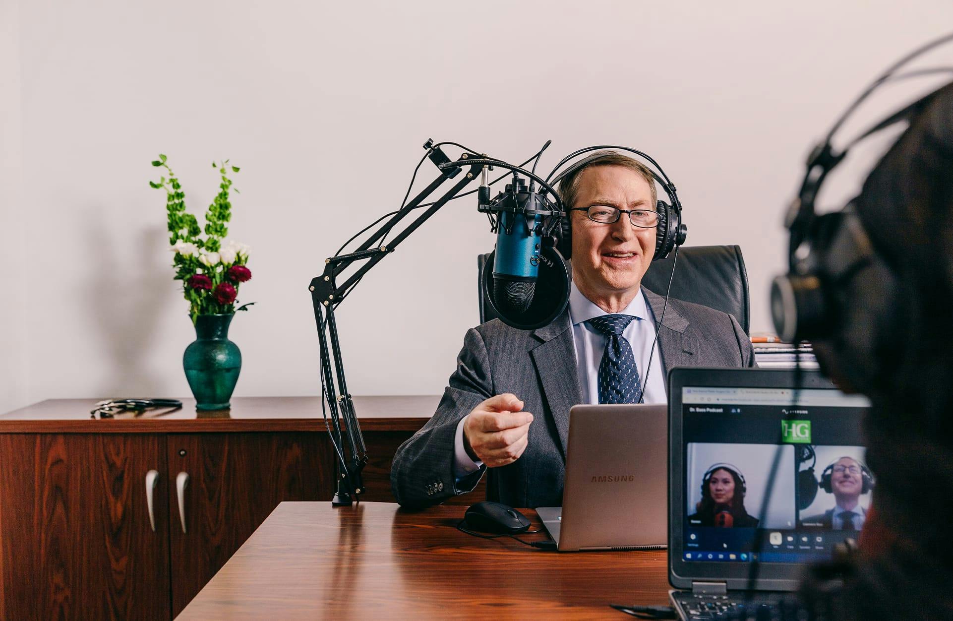 a photo of Dr. Bass in a suit doing a podcast with microphones and headphones