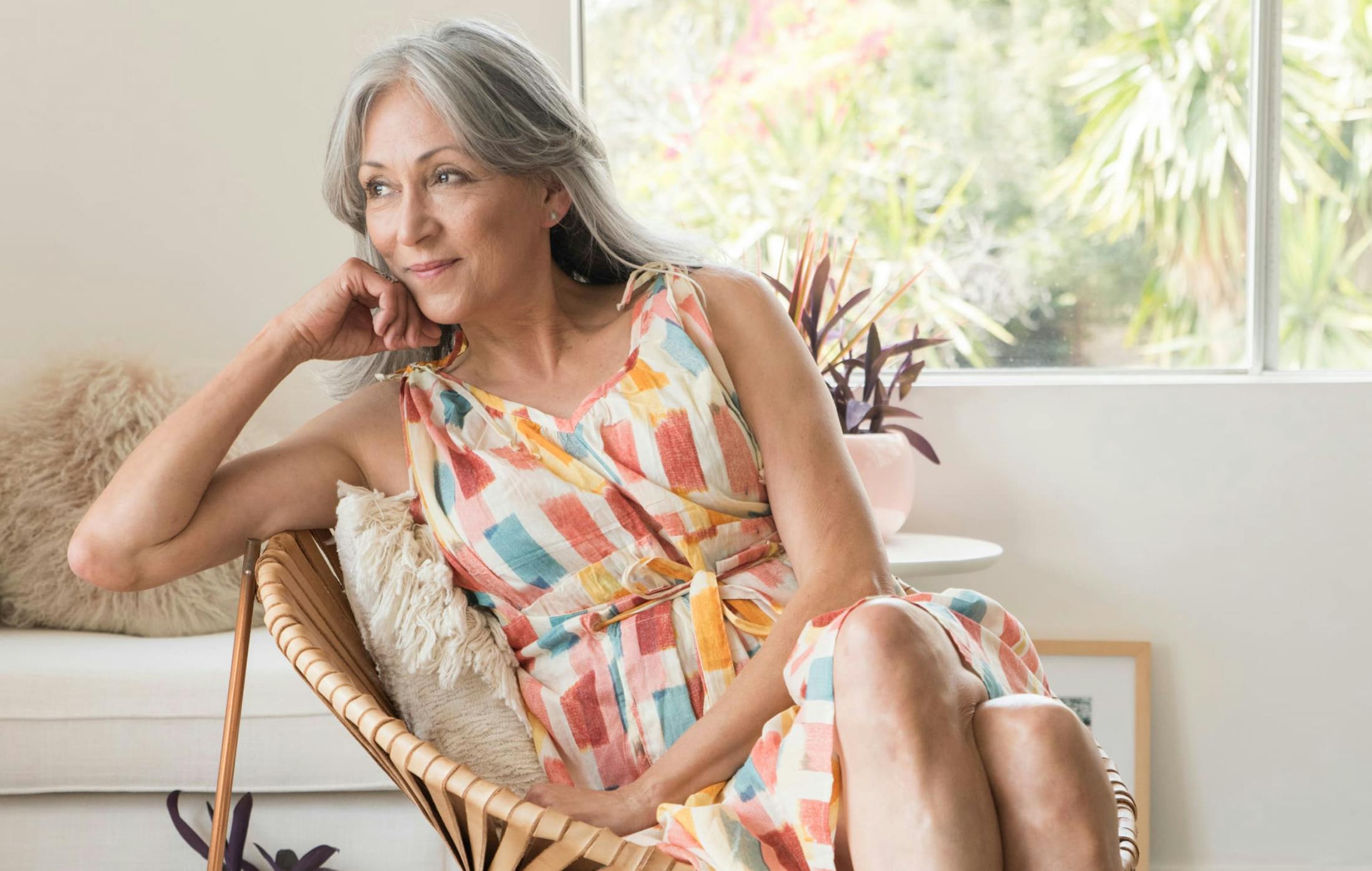 older woman in a colorful dress sitting on a chair smiling.
