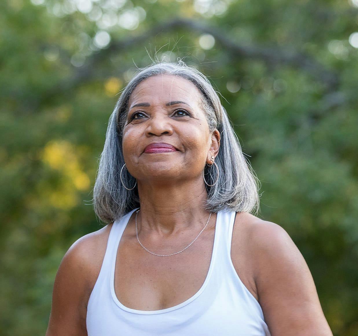 woman with gray hair and a white tank top and trees in the background