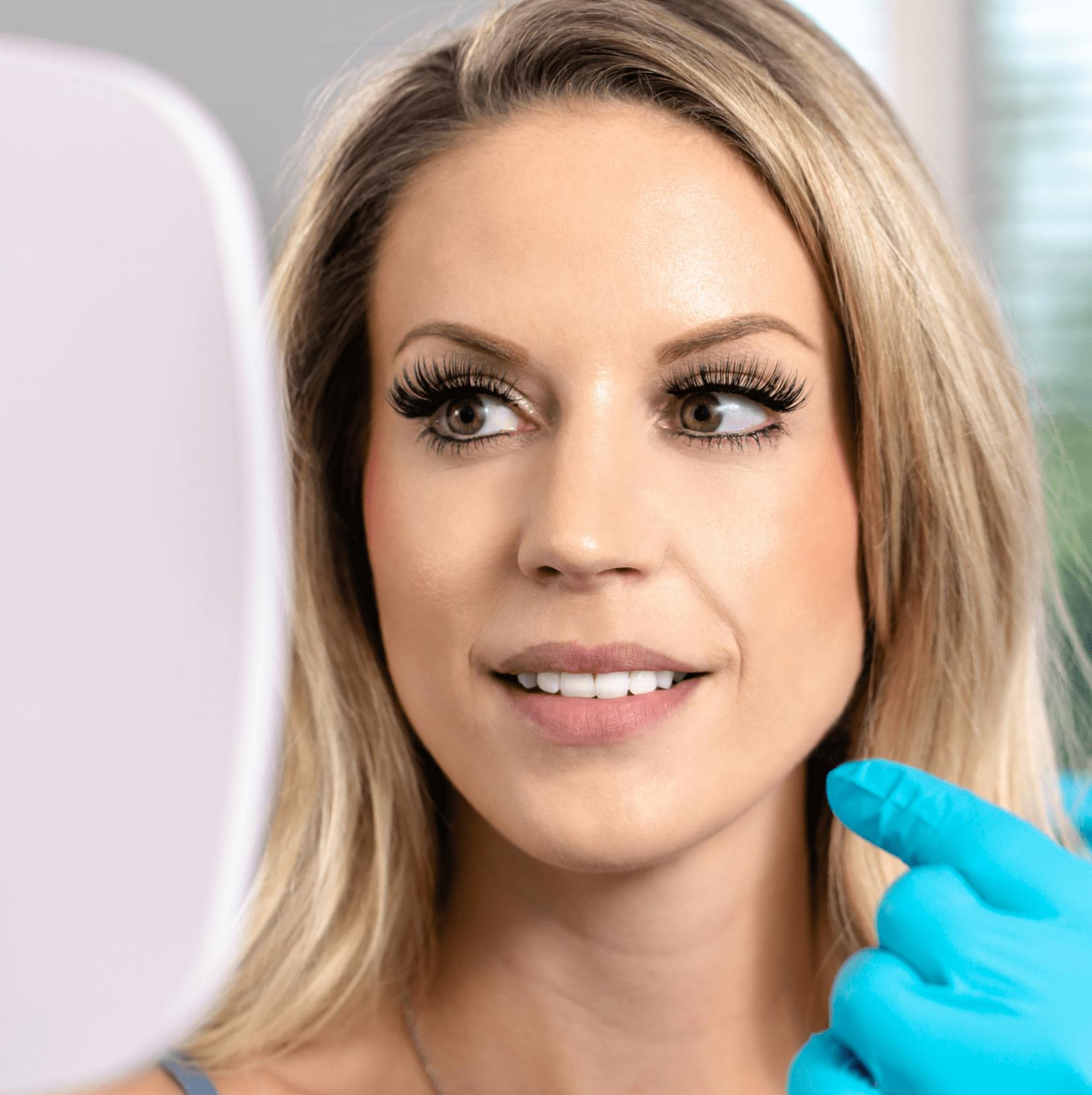 blond woman with blue gloves holding a mirror and smiling