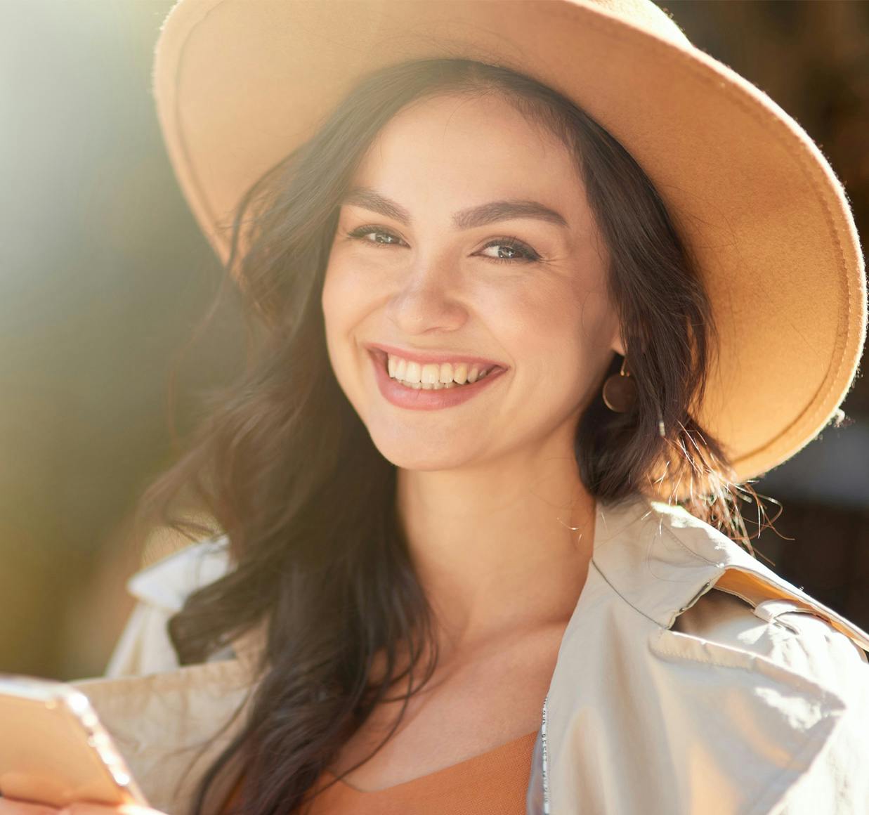 smiling woman in hat looking at her cell phone while standing outside