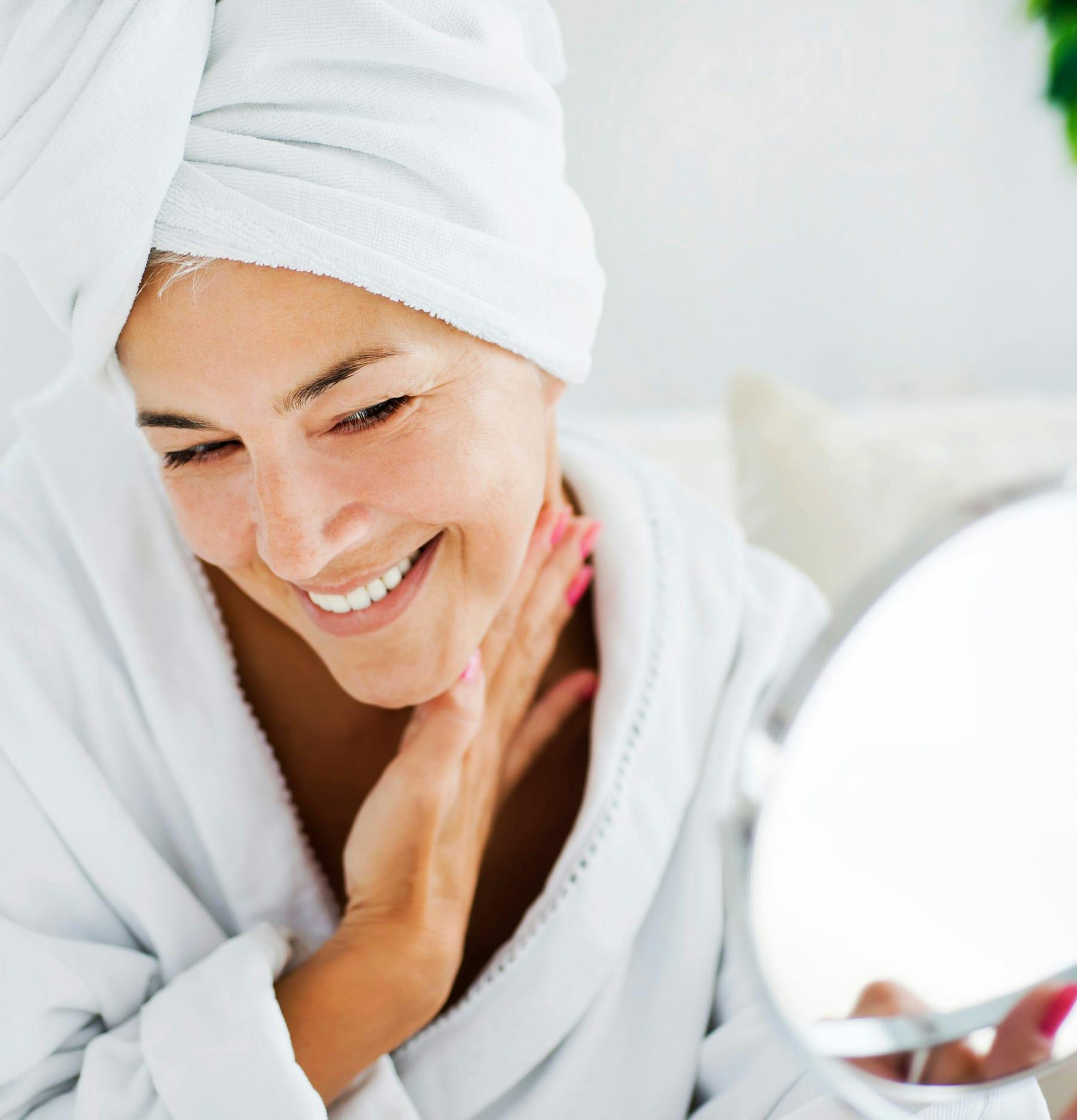 Woman wearing a robe and towel on her hair looking in a mirror