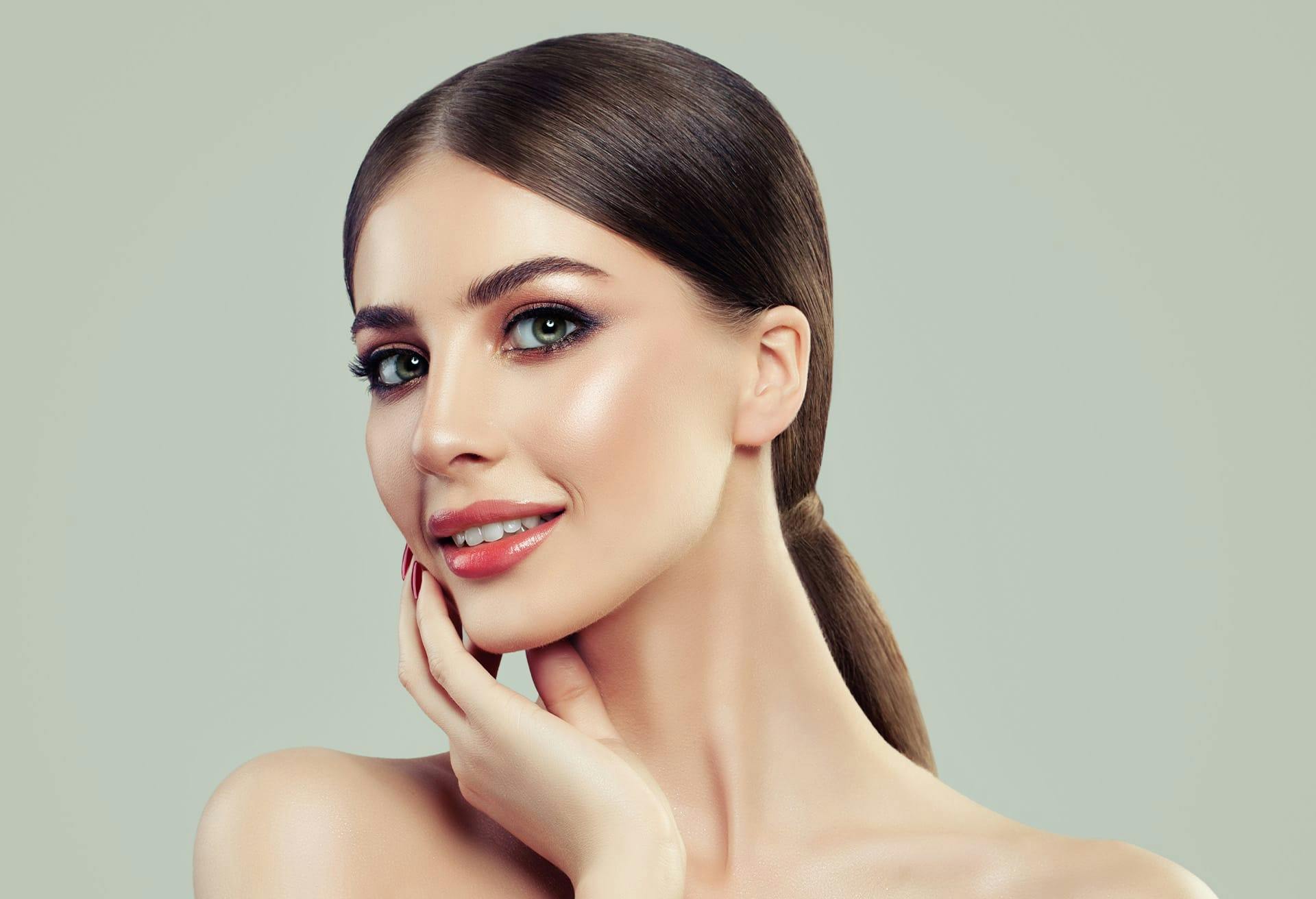 Woman with her dark hair in a slicked back ponytail touching her lower face
