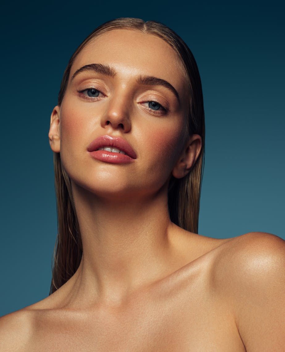 Close up of young woman's face and nack with perfect glowing skin. Her hair is slciked back. Her beatiful skin is to emulate the potential results of Toskani Skincare in Austin, TX with APSI