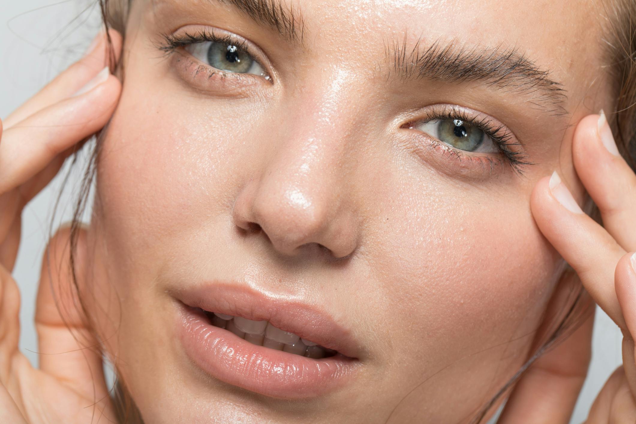 Close up of young woman's face with perfect skin. Her hands rest gently around her face. Her beatiful skin is to emulate the potential results of Toskani Skincare in Austin, TX with APSI