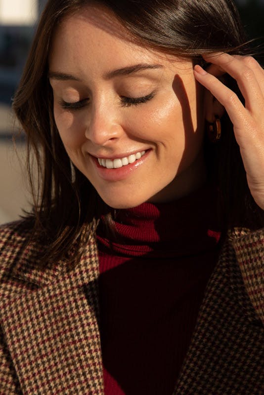 Woman smiling, looking down, with her hand running through her hair.