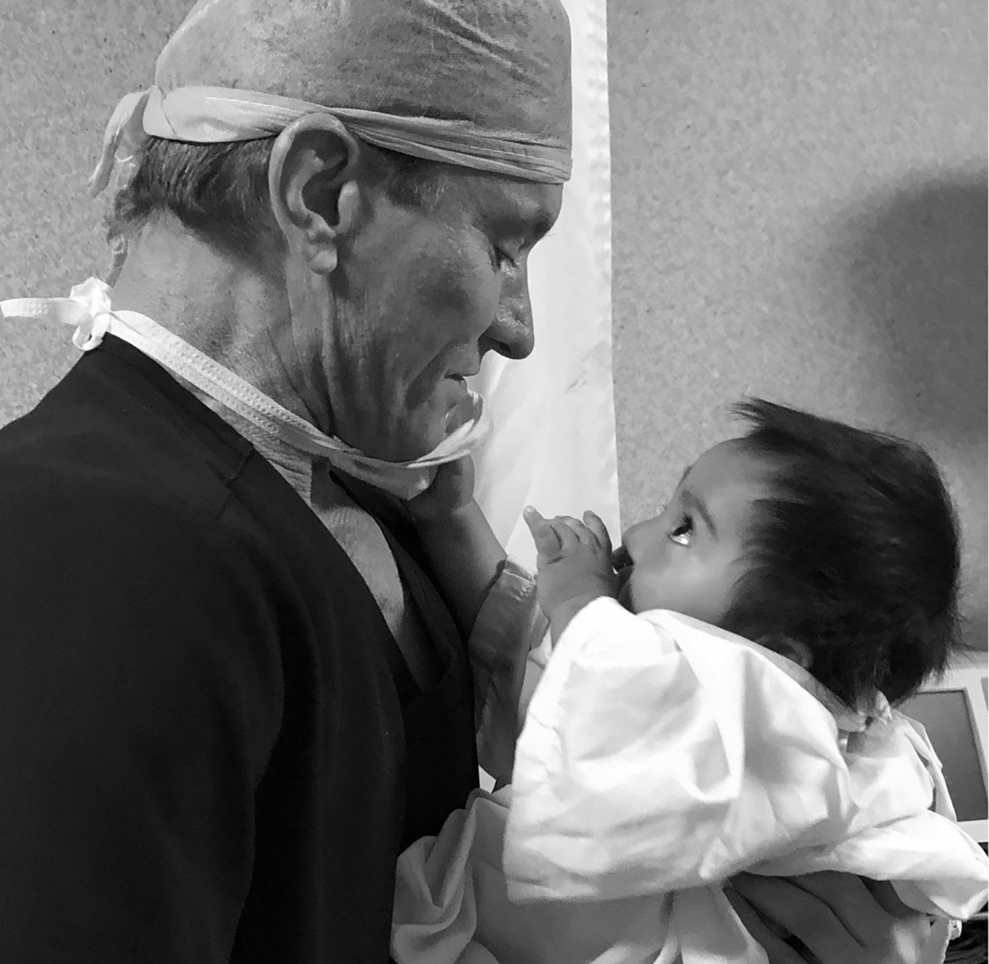 Black and white image of Dr. Shapiro hold and looking at a baby.