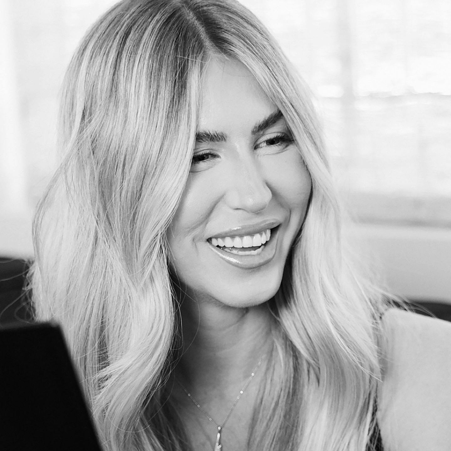 Black and white close up image of woman smiling, looking at something off camera.