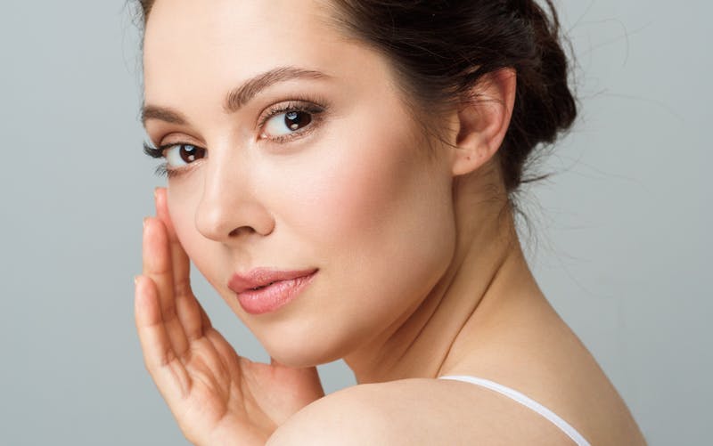 woman looking at camera resting hand near cheek, clean skin and natural makeup