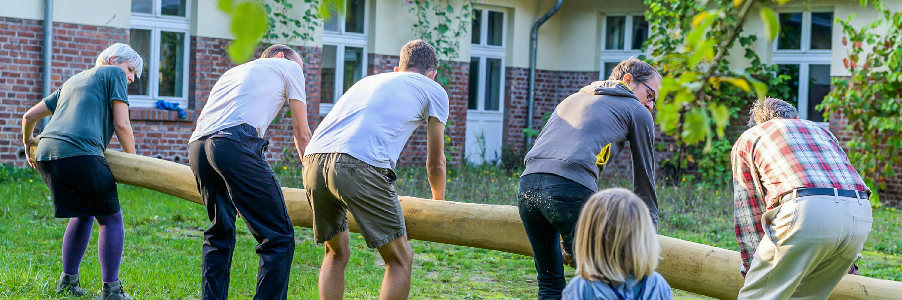 Community hilft beim Tragen von Robinie bei Spieplatzbau-Beteiligungsprojekt
