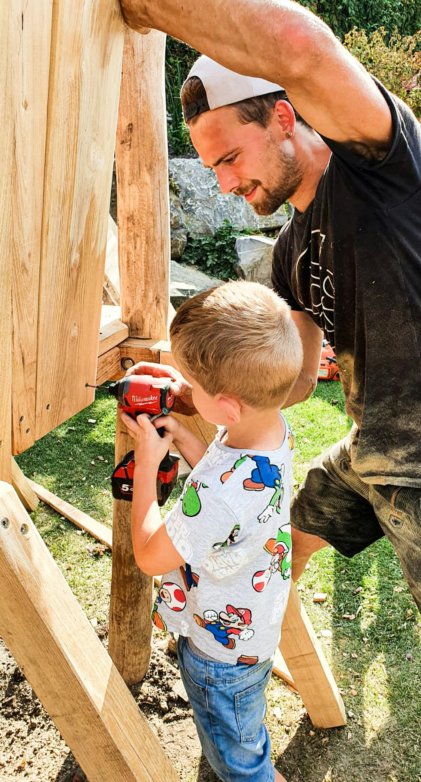 tollerei Mitarbeiter schraubt mit Kind eine Schraube in den Spielplatz