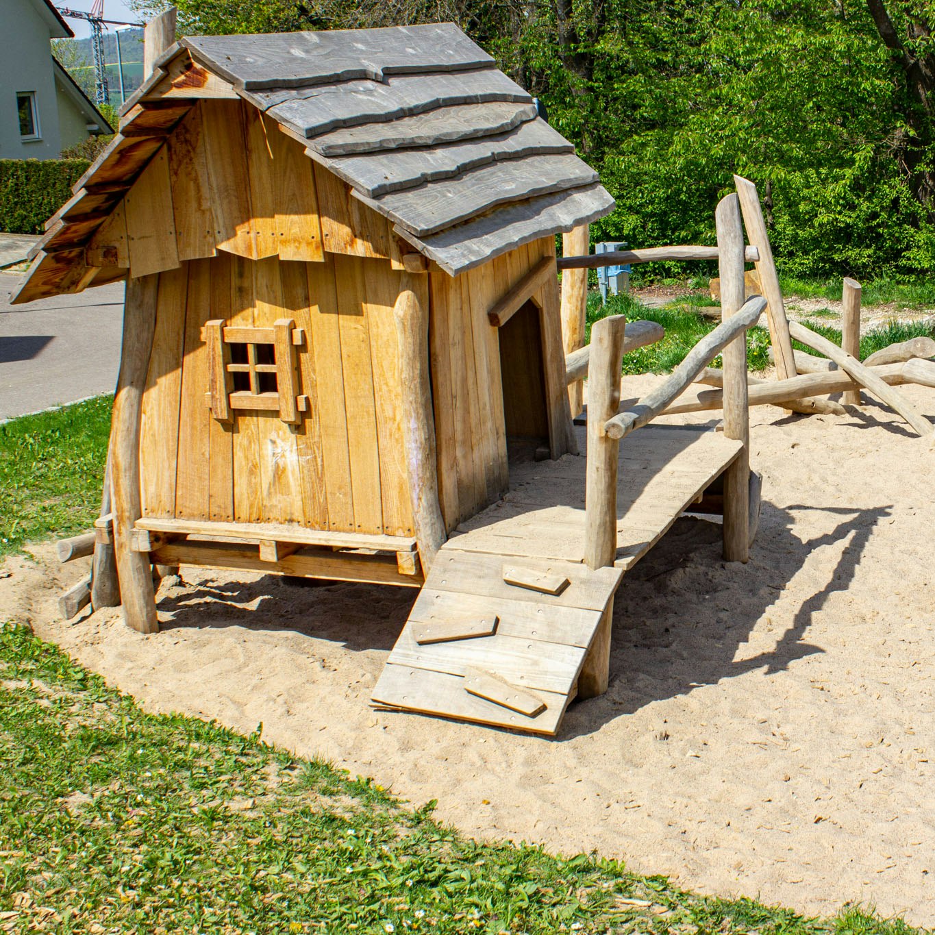 Ein Häuschen aus Holz mit Sandkasten und Kletterbalken
