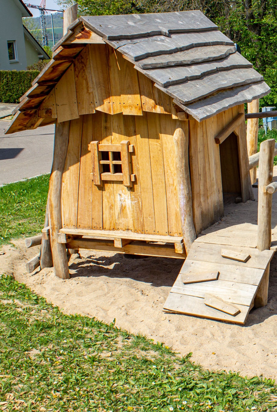 Ein Häuschen aus Holz mit Sandkasten und Kletterbalken