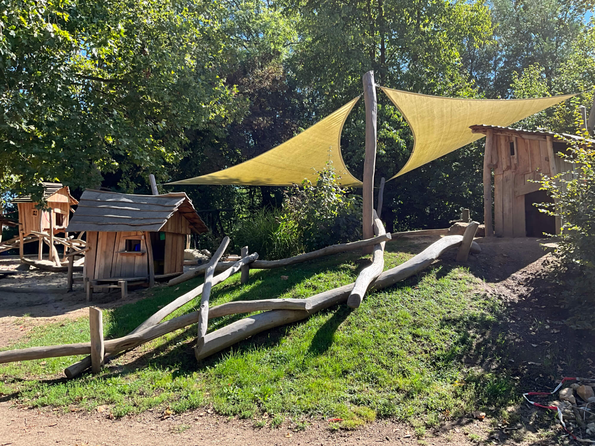 Eine Spielhütte mit Sonnensegel in einem Waldgebiet.