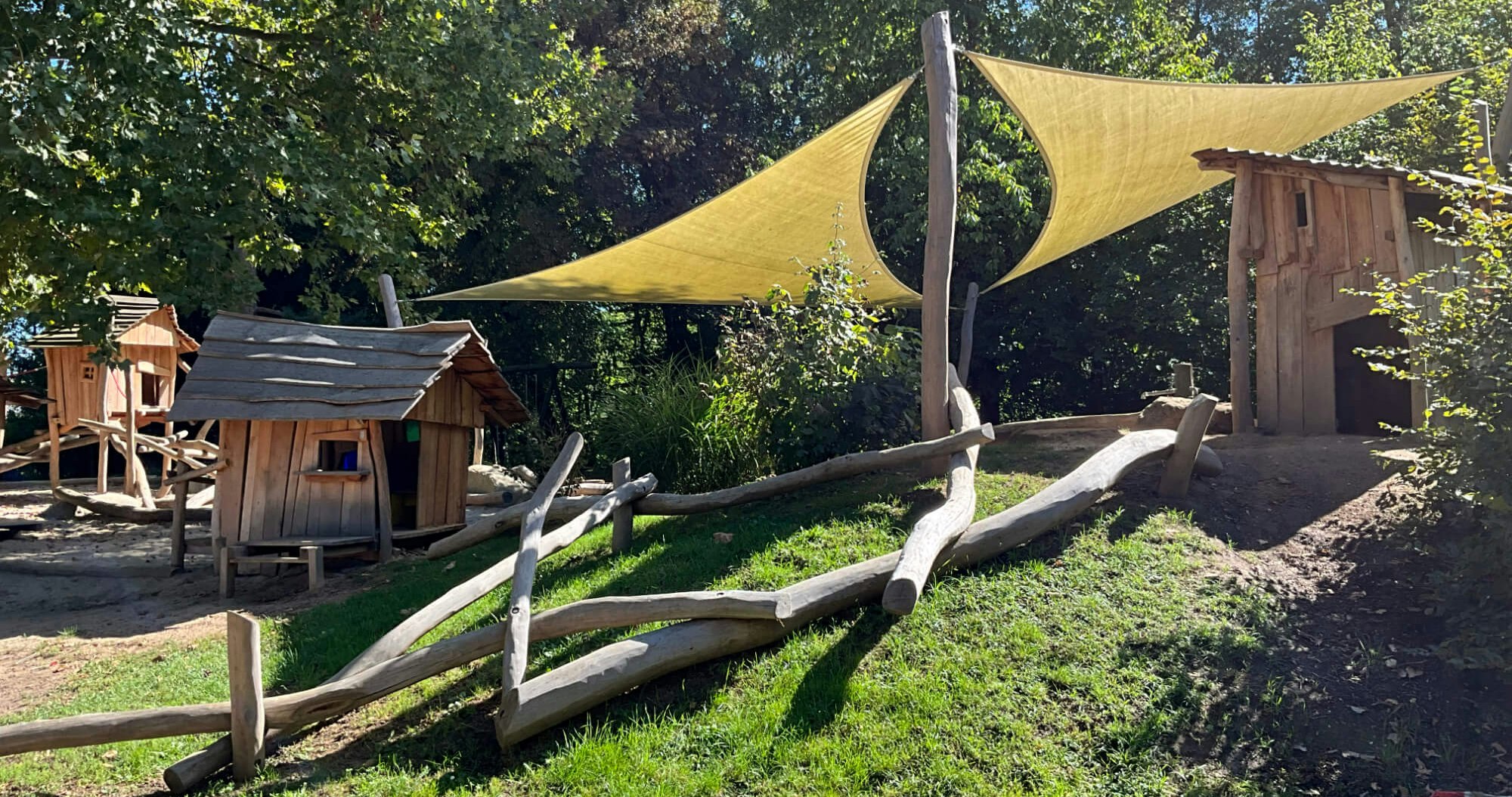 Eine Spielhütte mit Sonnensegel in einem Waldgebiet.