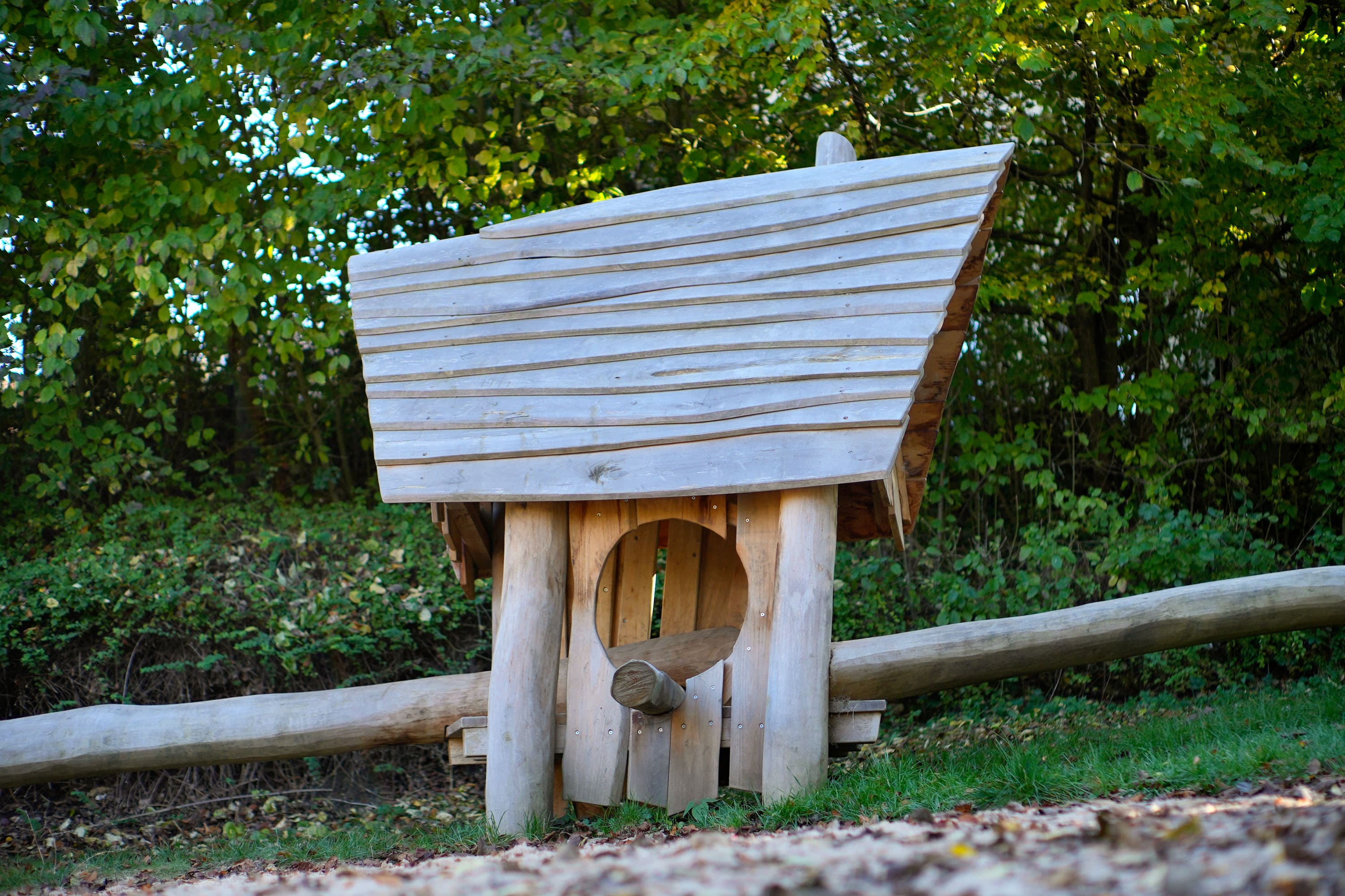 Eine kleine Holzhütte mit schrägem Dach liegt in einer Grasfläche, umgeben von üppigem Grün und Bäumen.