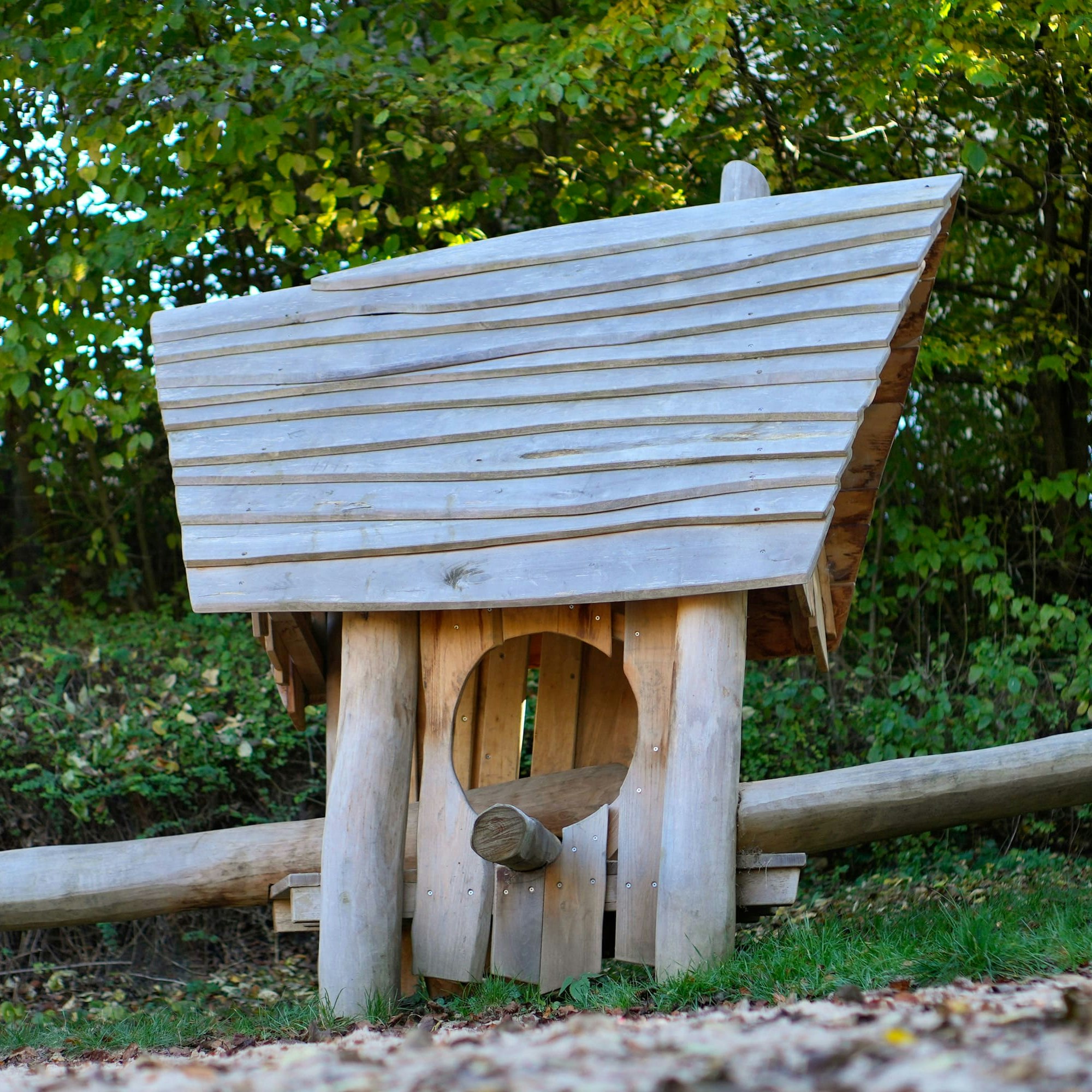 Eine kleine Holzhütte mit schrägem Dach liegt in einer Grasfläche, umgeben von üppigem Grün und Bäumen.