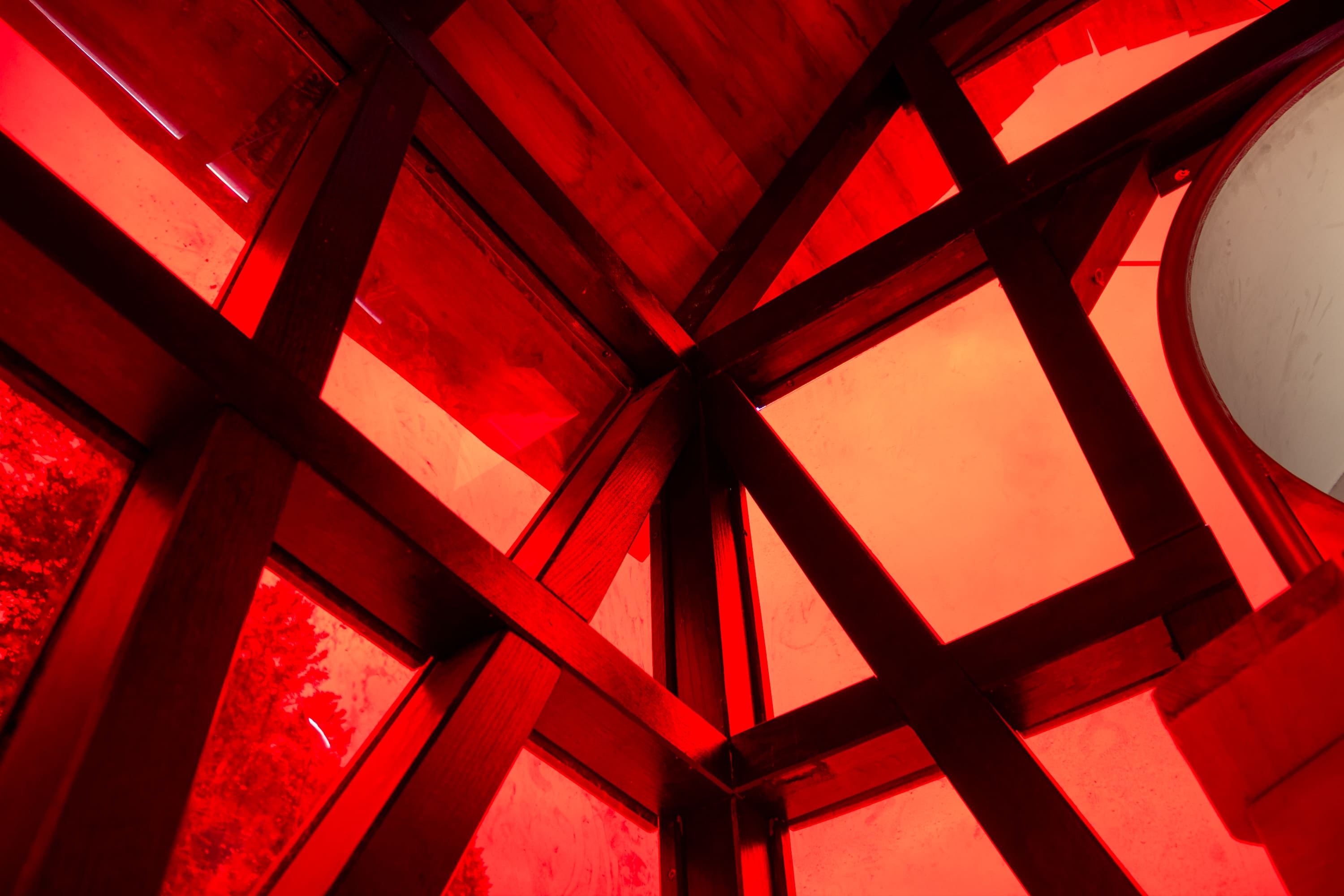 Holzbalken kreuzen sich mit rot getönten Platten in einer geometrischen Deckenstruktur und erzeugen ein kräftiges Muster aus Linien und Formen.