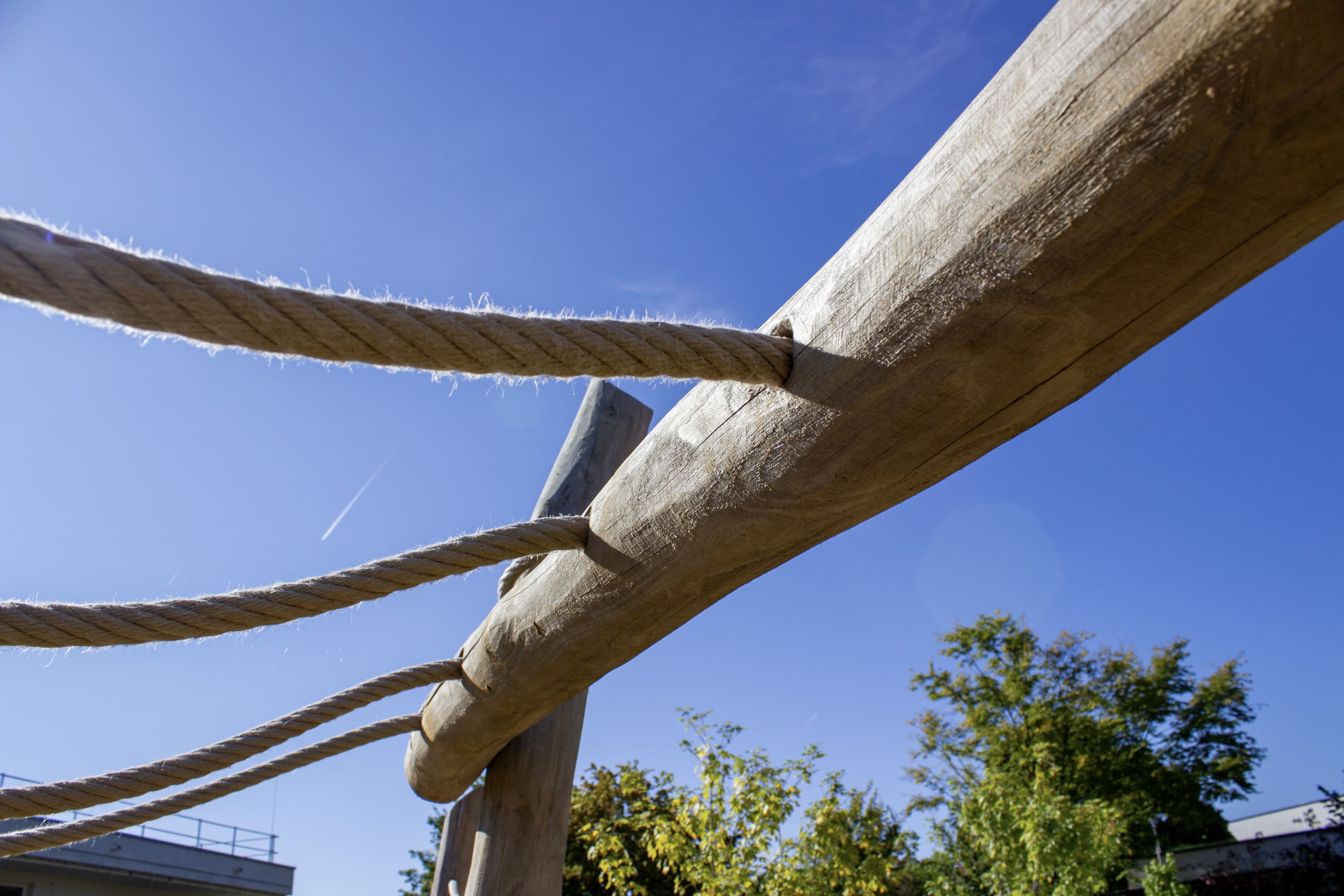 Nahaufnahme von dicken Seilen, die zwischen großen Holzbalken verknotet sind, mit einem klaren blauen Himmel und einigen Bäumen im Hintergrund.