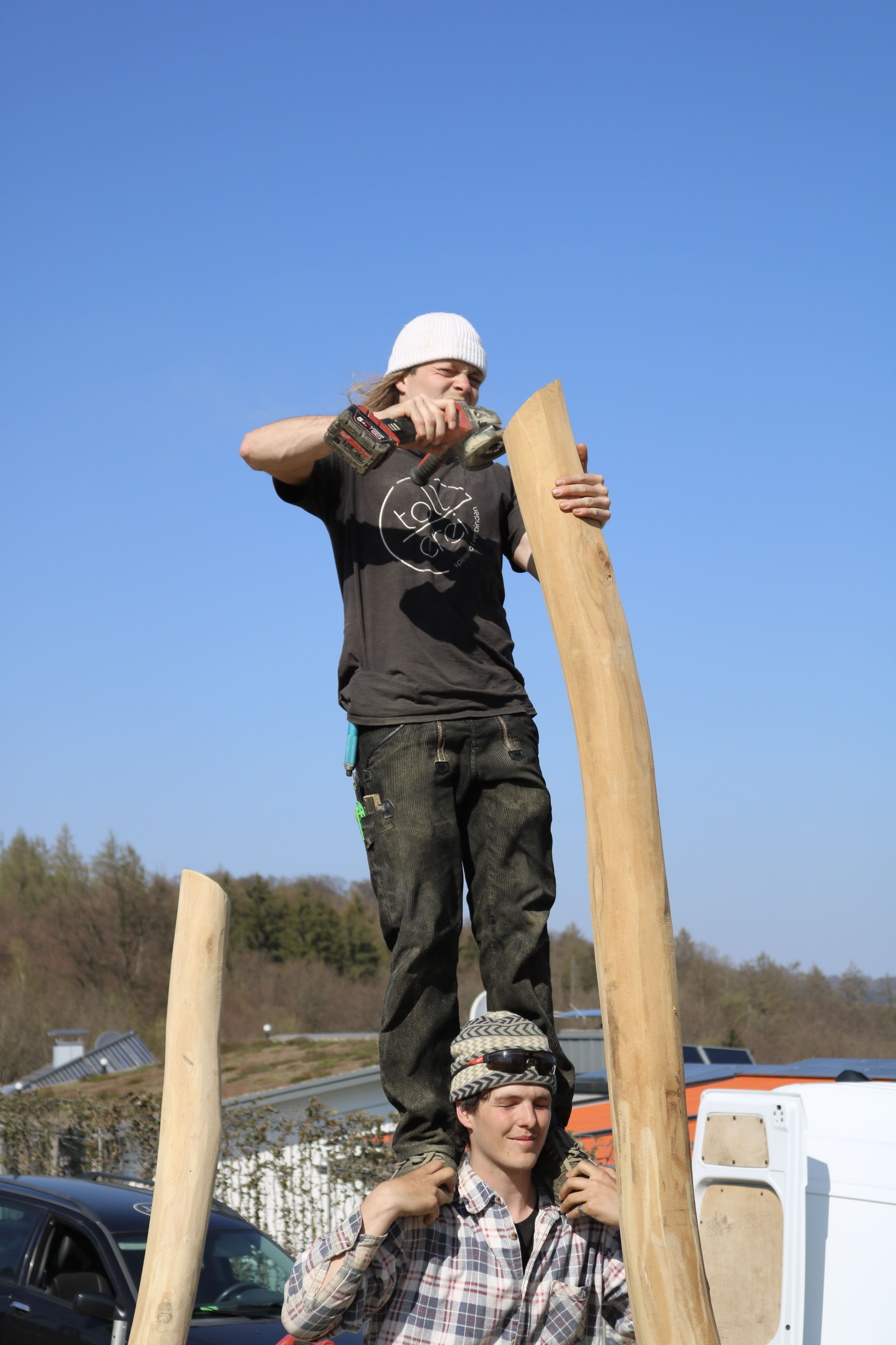 Eine Person steht auf den Schultern einer anderen Person und bohrt an einem sonnigen Tag im Freien in einen Stamm.