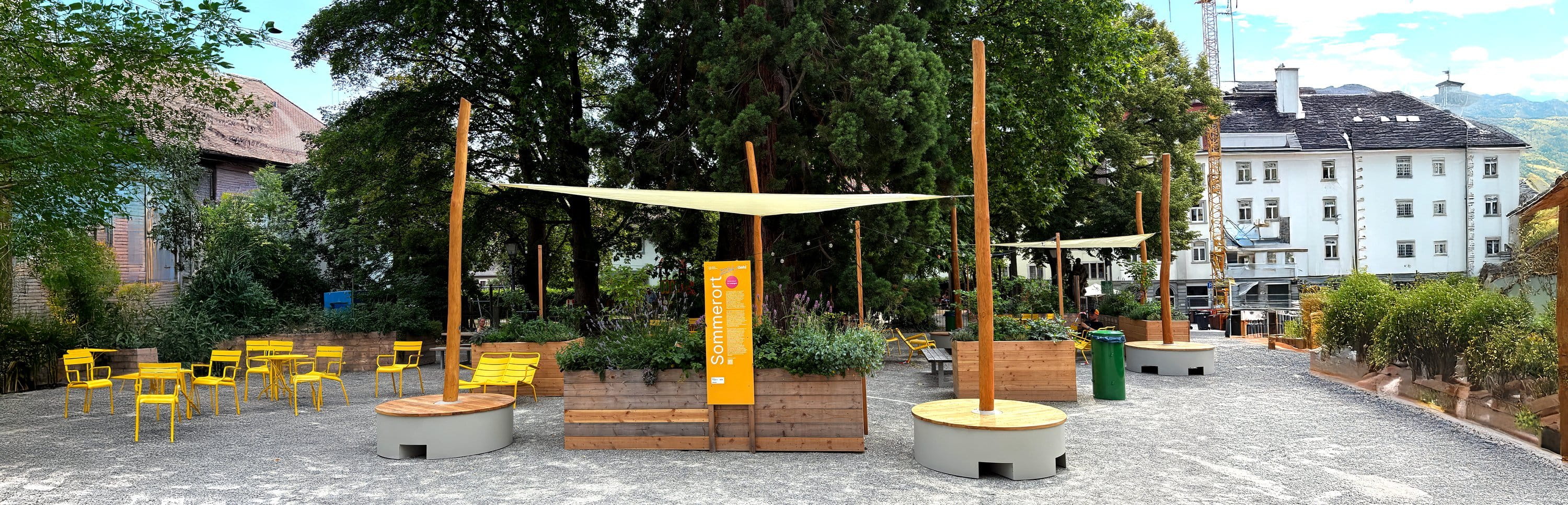Stadtplatz mit POP-UP-Sonnensegeln, Hochbeeten, gelben Stühlen und einer orangefarbenen Sommerort-Stele.