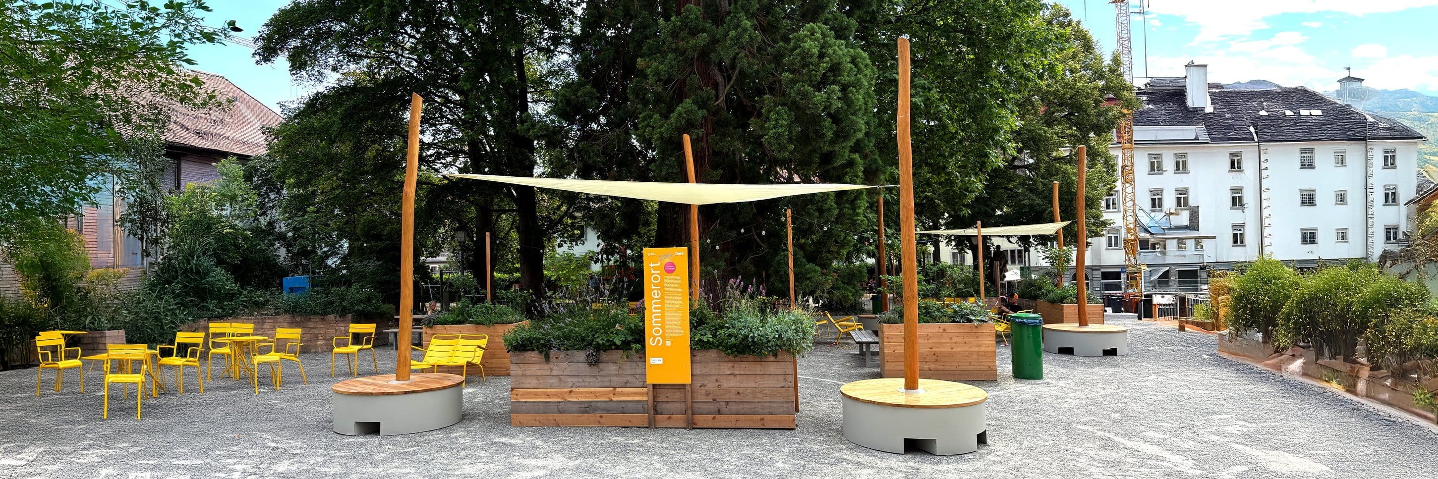 Stadtplatz mit POP-UP-Sonnensegeln, Hochbeeten, gelben Stühlen und einer orangefarbenen Sommerort-Stele.
