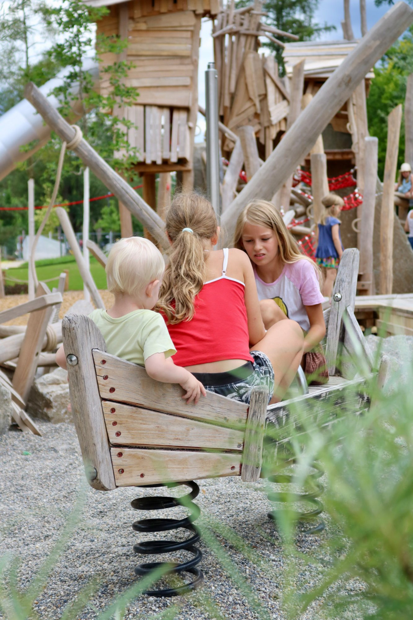 Drei Kinder sitzen gemeinsam in einem hölzernen Federwipp-Boot auf dem Piratenspielplatz in Tübingen.