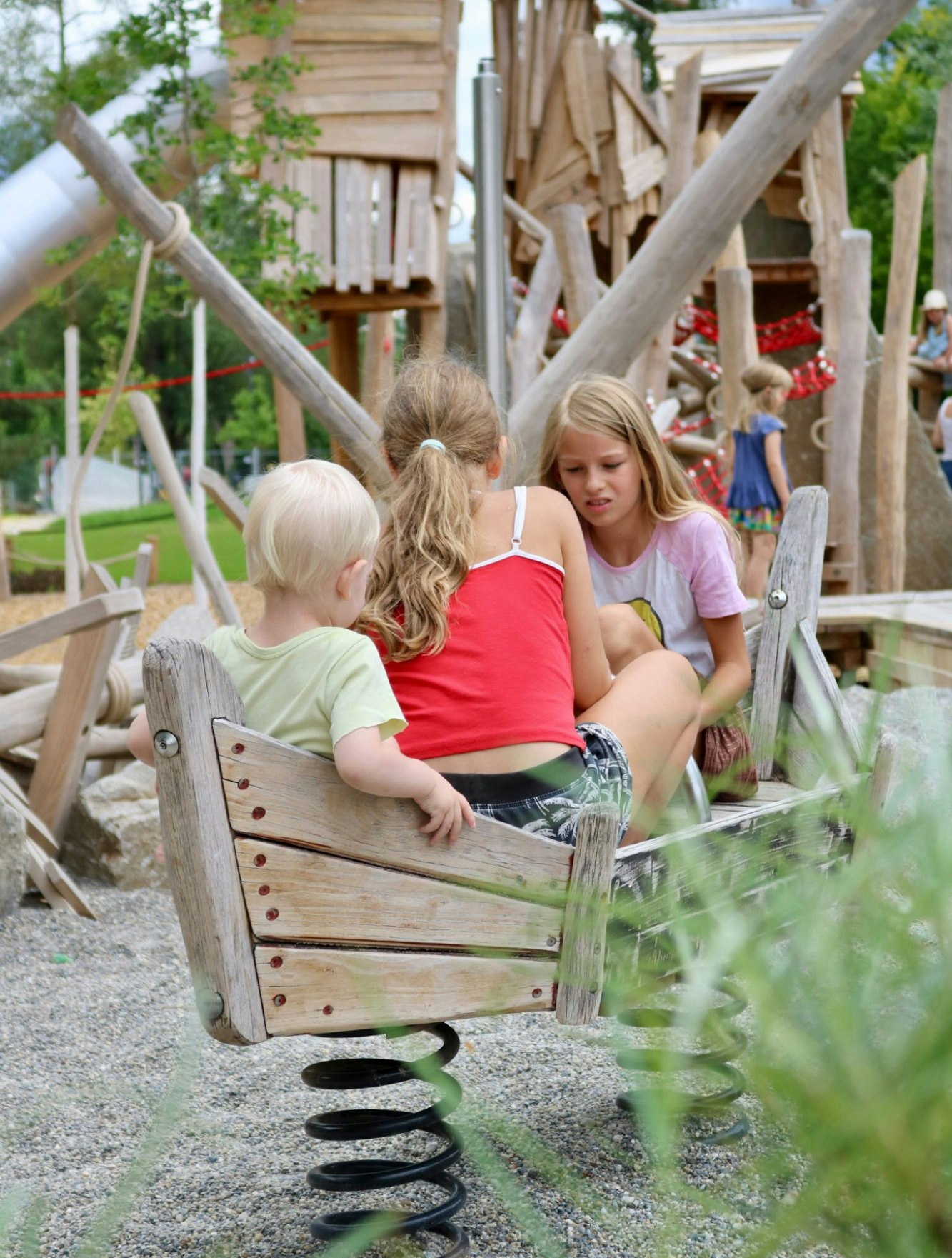 Drei Kinder sitzen gemeinsam in einem hölzernen Federwipp-Boot auf dem Piratenspielplatz in Tübingen.