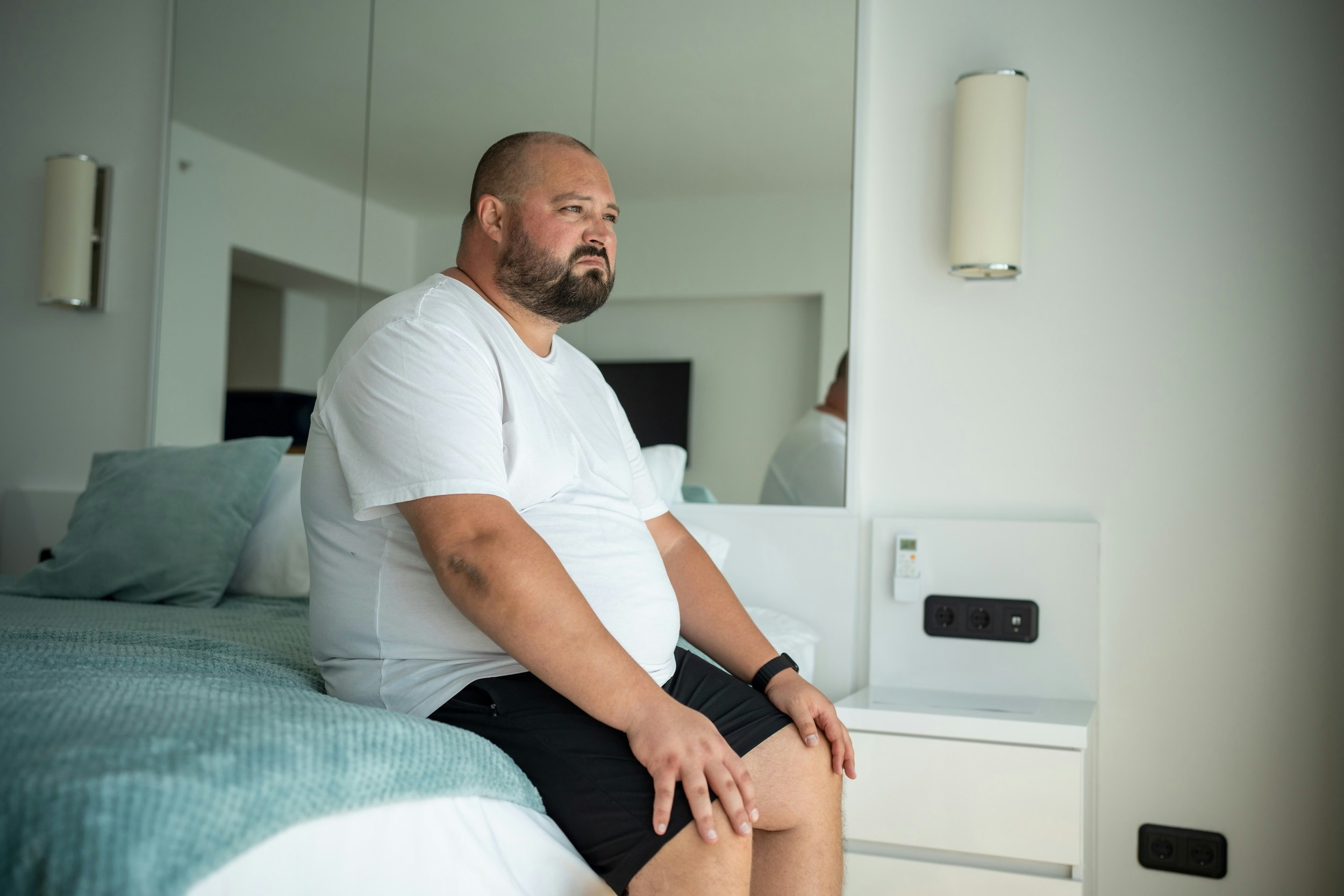 Mand i soveværelse kigger ud af vindue