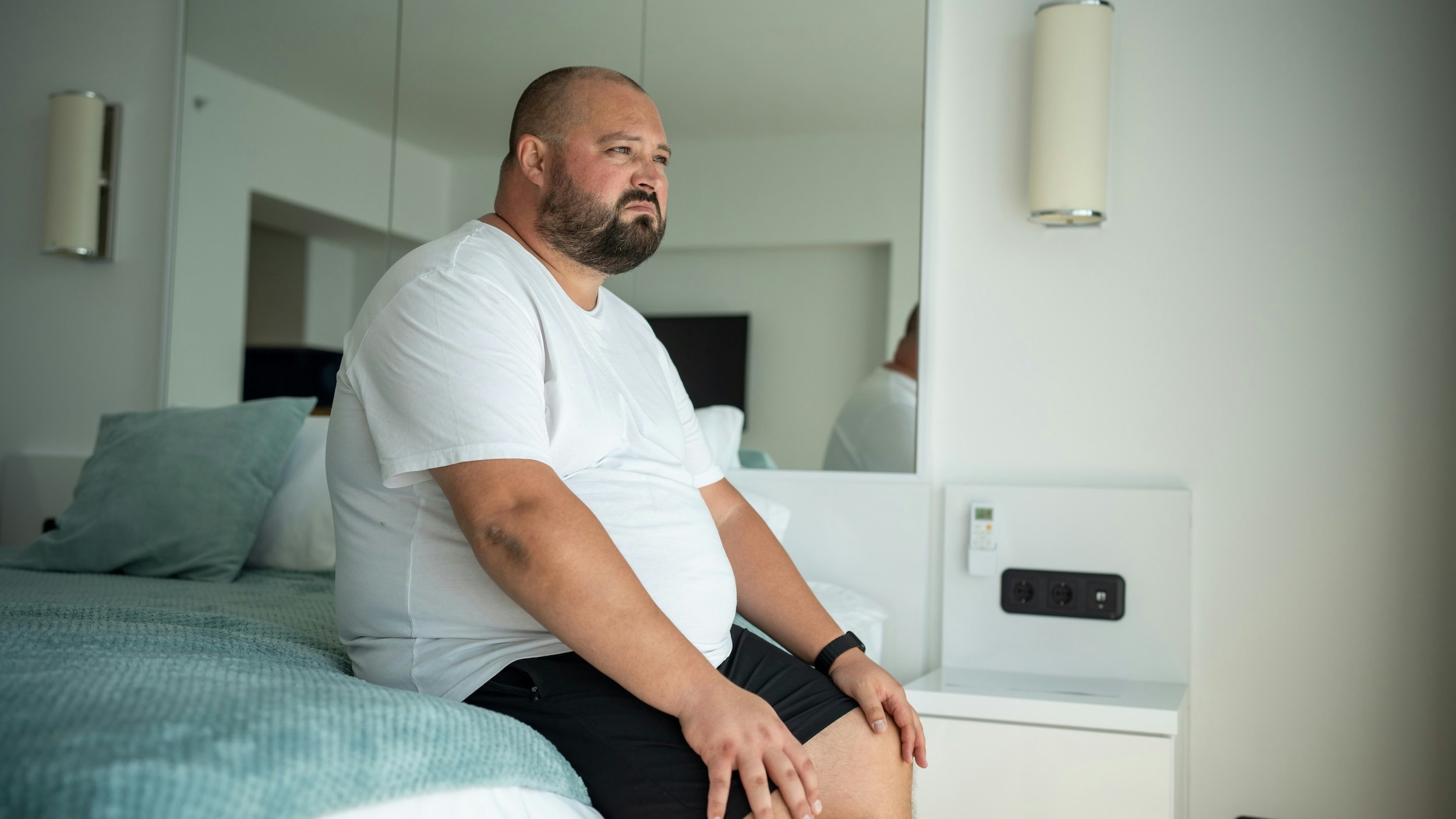 Mand i soveværelse kigger ud af vindue