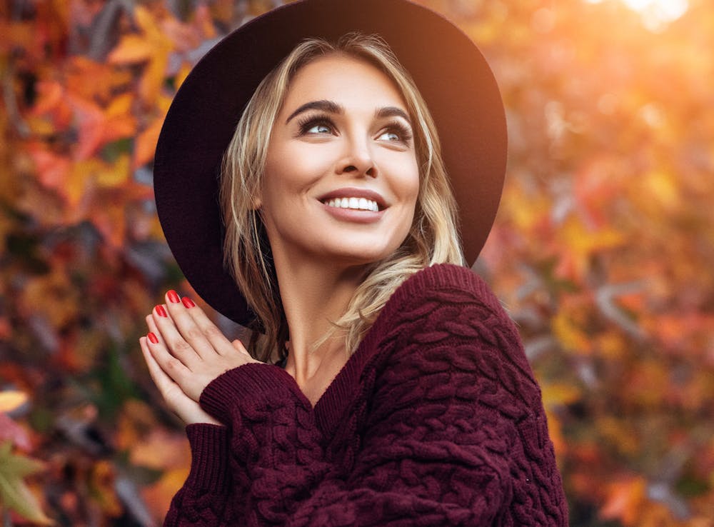 Woman wearing a hat with sun and trees in the background.