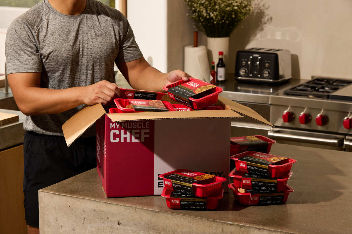 Man enjoying a healthy meal with chicken, broccoli, and sweet potatoes, alongside a My Muscle Chef meal package.