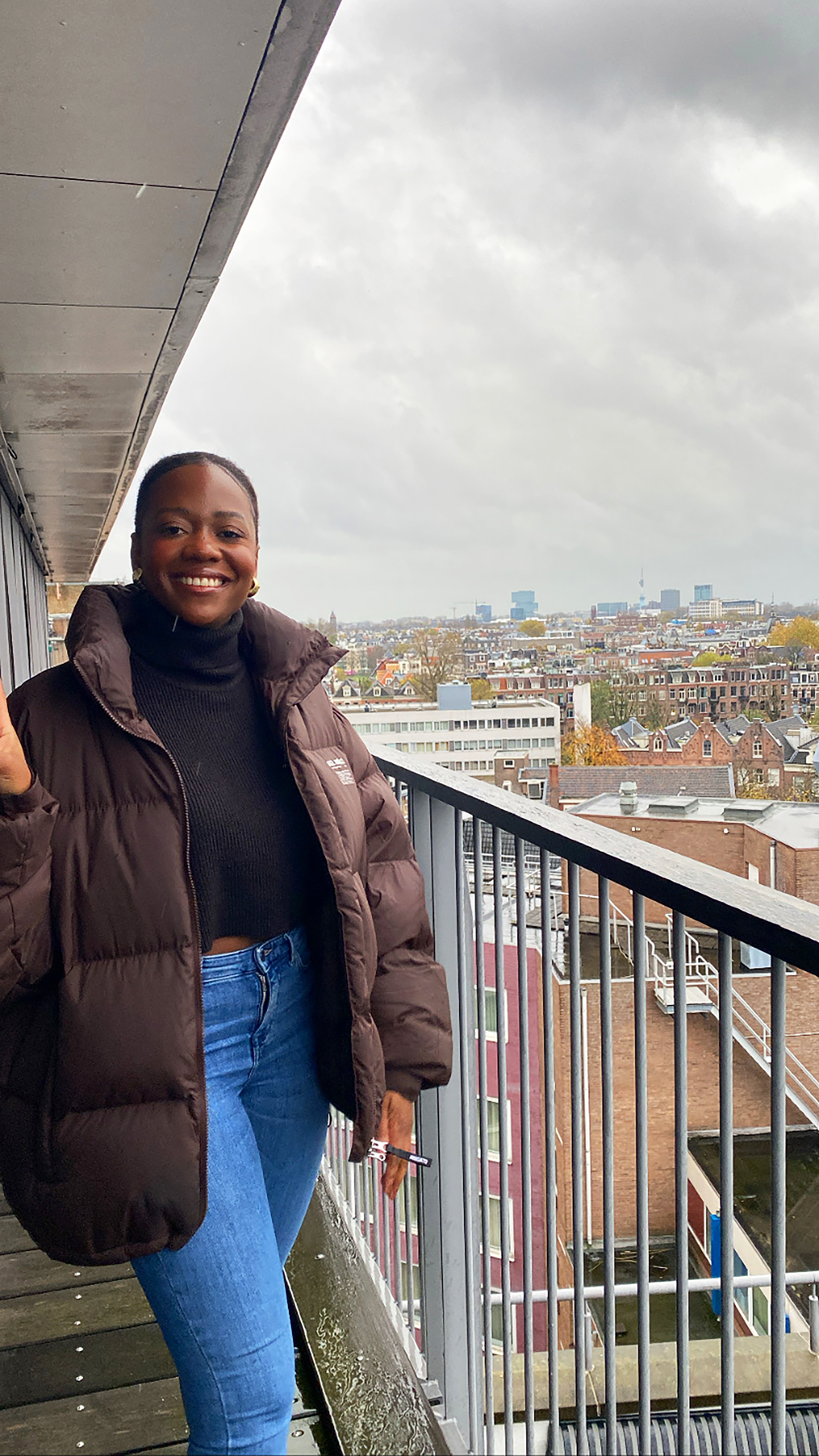 Nainen tervehtii parvekkeelta, joka on korkealla. Taustalla näkyy Amsterdamin maisema.