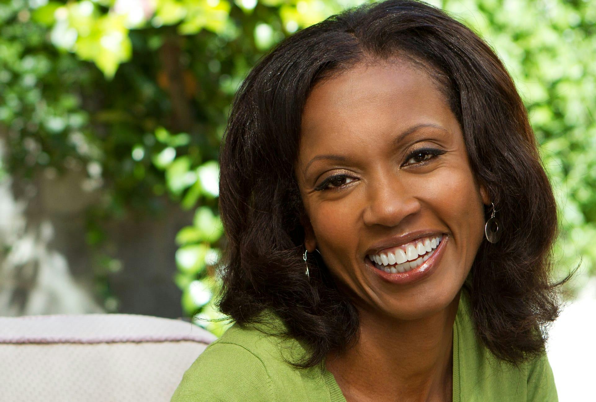 Woman Smiling with Green Sweater and Green Trees in the Background