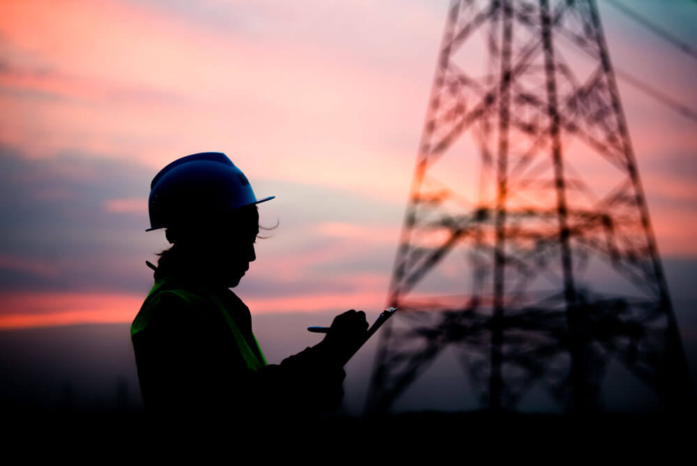 worker in front of electricity mast at sunset
