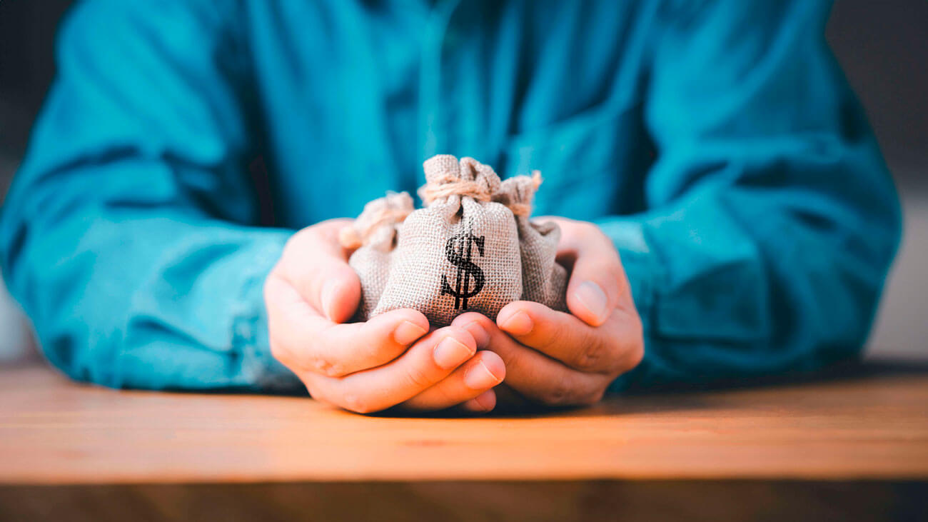 man sitting at table with small bags of money