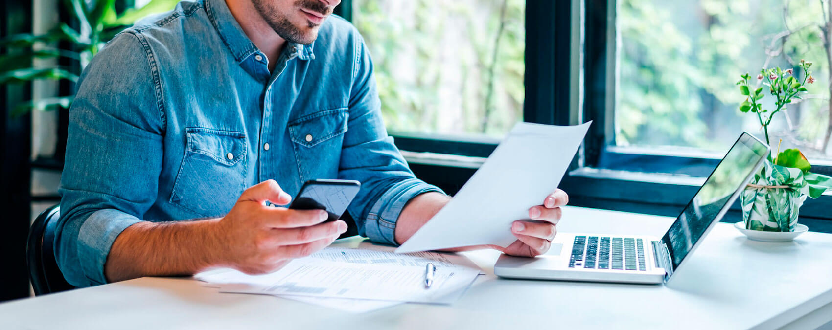 man sitting at table with laptop, phone, and papers