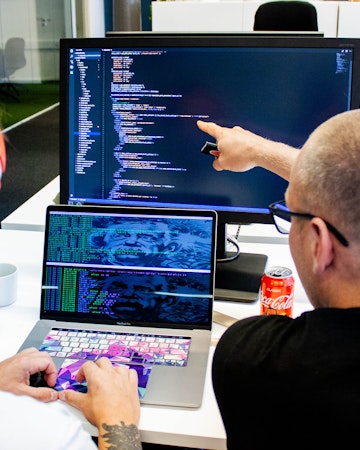 två personer diskuterar kod framför en skärm med kod