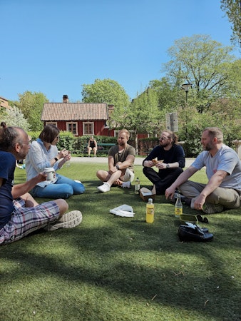 Kollegor som äter lunch tillsammas i solen på gräs