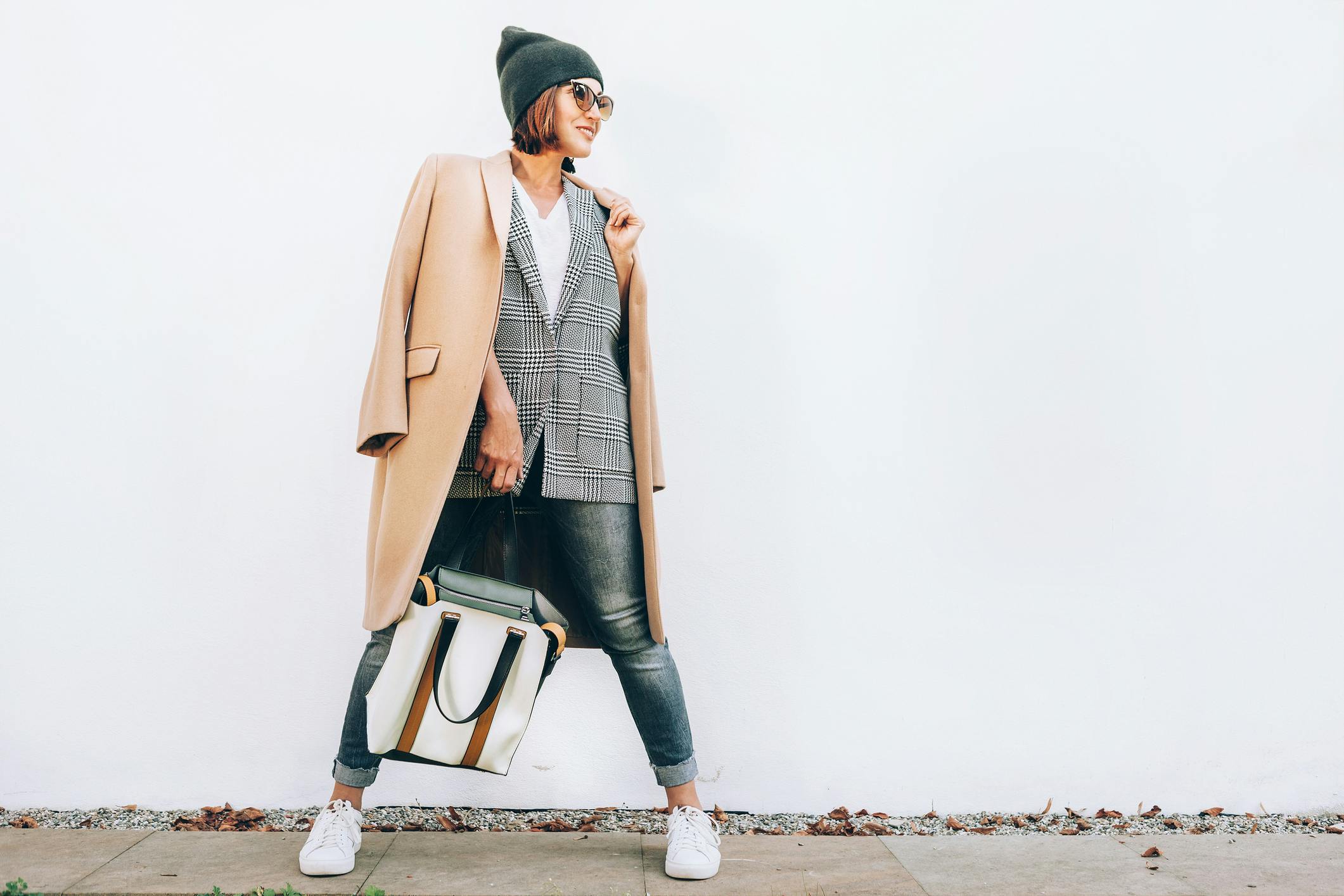 woman wearing a coat, sweater, jeans and sneakers standing on a sidewalk