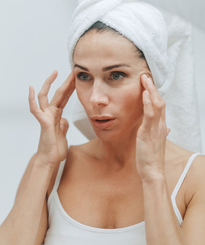 A woman in her 50s examining her face and pulling her face back