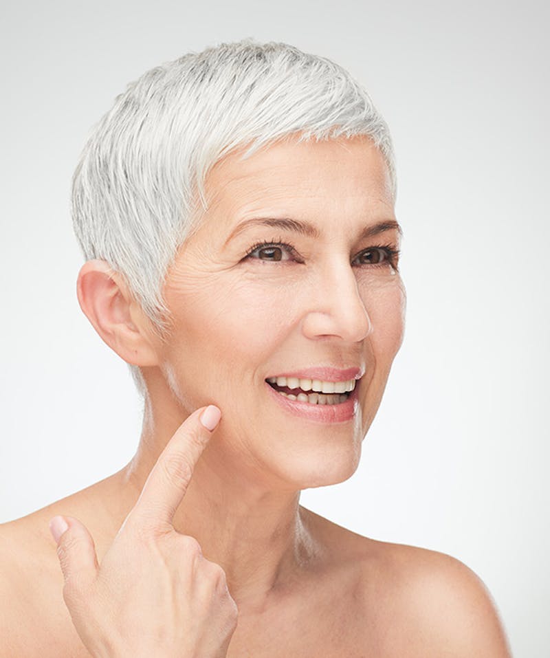 A woman in her 50s looking at and pointing to her wrinkles